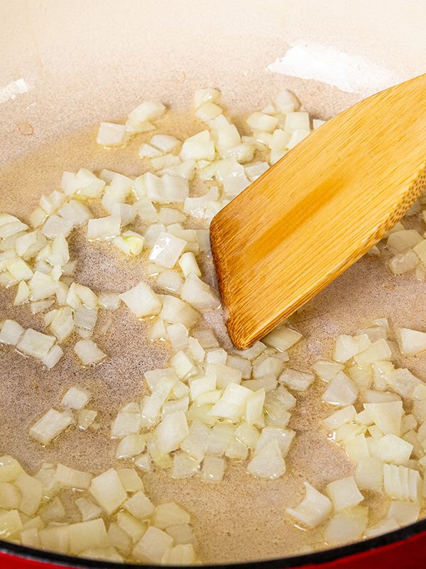 Diced onions sautéing in oil in a large red skillet to start the chicken mushroom alfredo sauce.