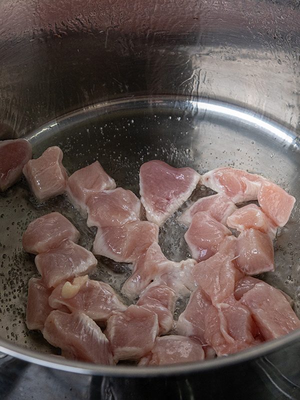 Cubed chicken breast sautéing in a large soup pot with oil.