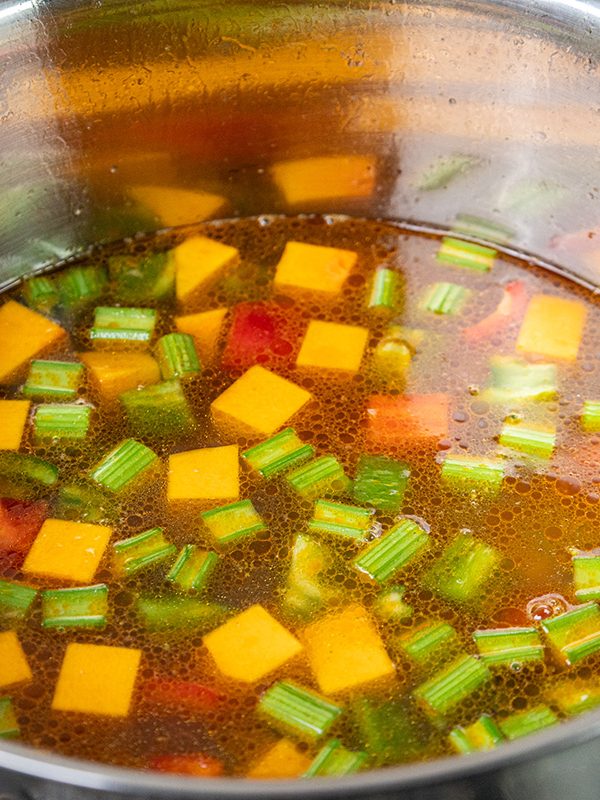 Chicken broth simmering with chicken, squash, celery, carrots, and peppers while cooking chicken vegetable soup recipe.
