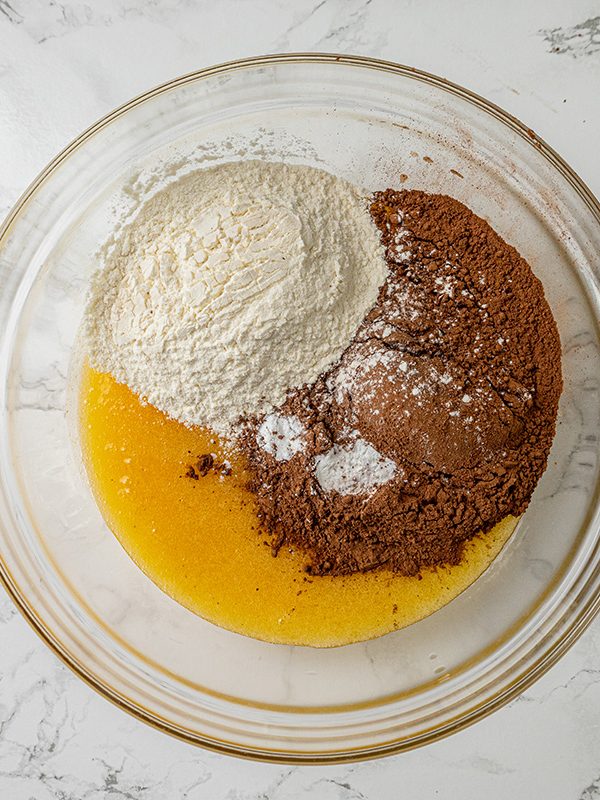 Flour, cocoa powder, and baking powder added on top of melted butter mixture in a mixing bowl.