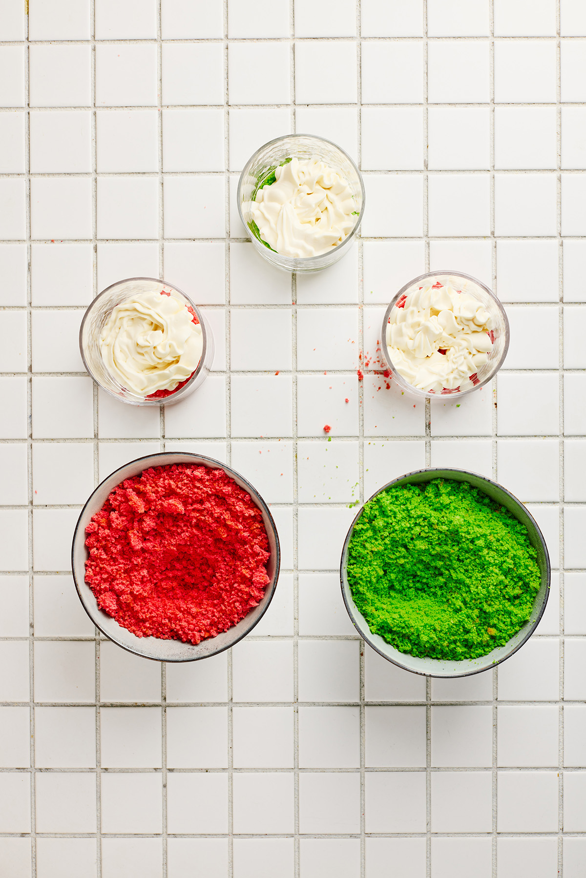 A fun and festive Christmas trifle dessert made with crumbled red and green cakes and an easy, fluffy cream cheese filling that tastes like the holidays in every bite. Small glasses filled with layers of red or green cake crumbs and piped cream mixture.