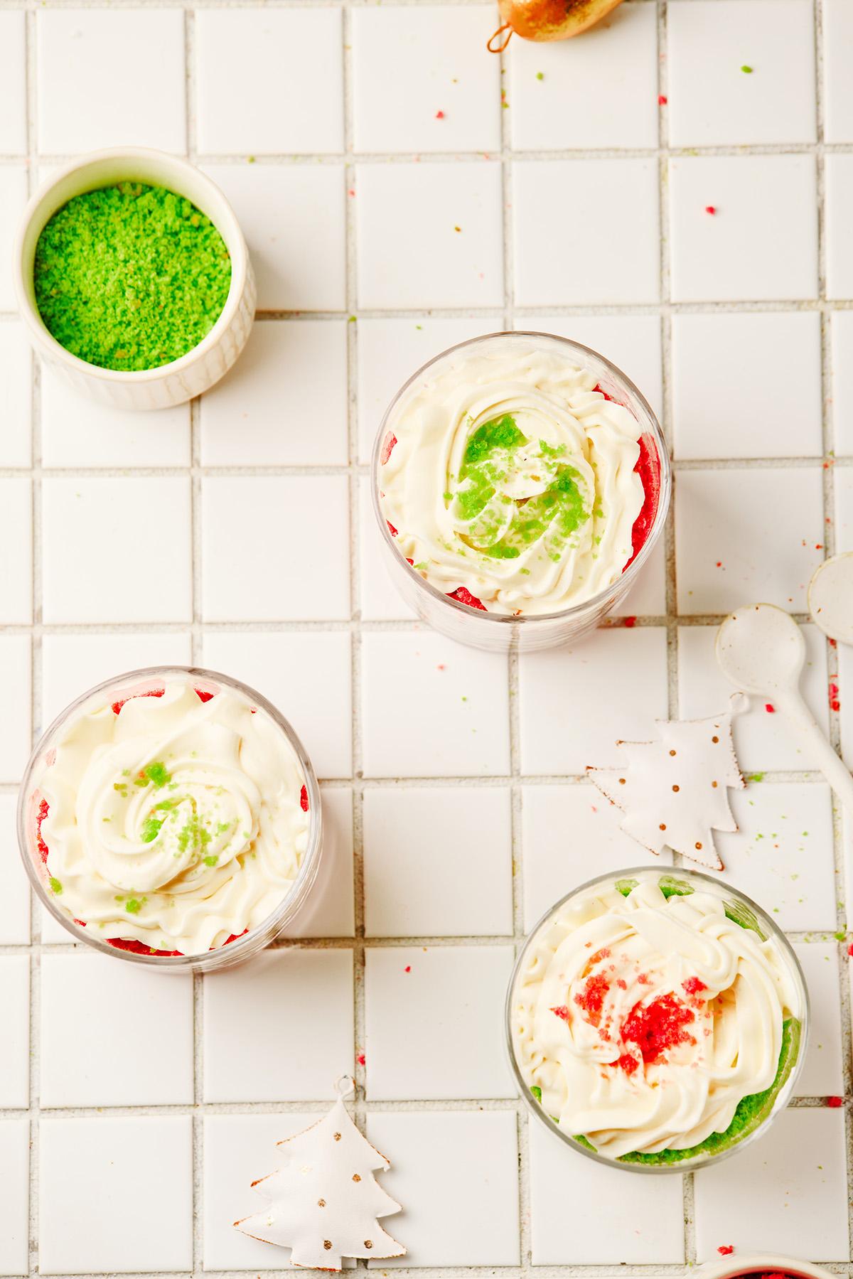 A fun and festive Christmas trifle dessert made with crumbled red and green cakes and an easy, fluffy cream cheese filling that tastes like the holidays in every bite. Mini Christmas trifles topped with piped cream and sprinkled with green cake crumbs