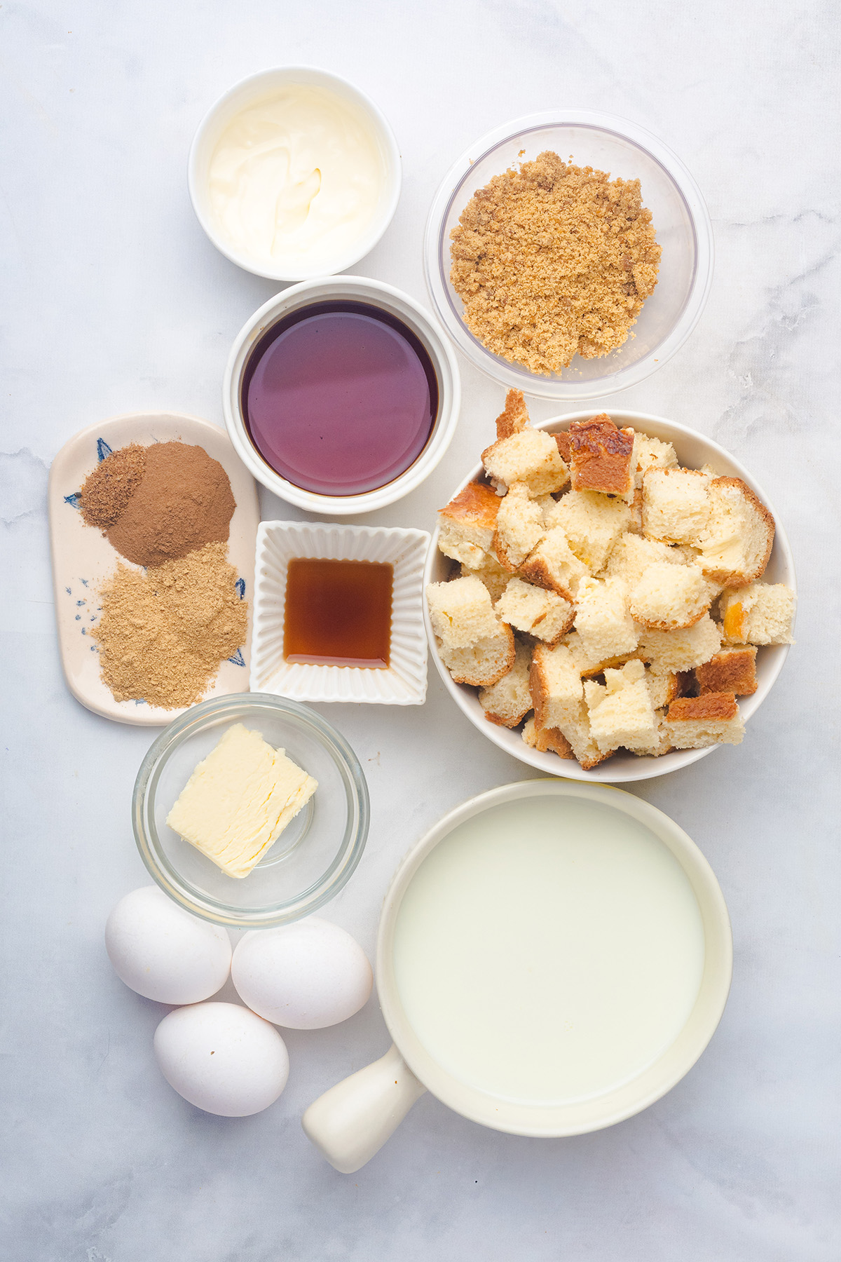 With rich molasses, warm spices, and a crunchy topping, this gingerbread French toast casserole is an easy, crowd-pleasing breakfast for Christmas morning. Ingredients for gingerbread French toast casserole arranged on a white surface, including cubed brioche, spices, molasses, brown sugar, eggs, milk, cream, and butter.