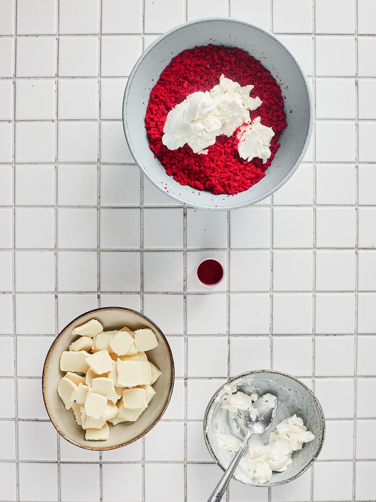 Bowl of crumbled red velvet cake topped with scoops of cream cheese frosting before mixing.