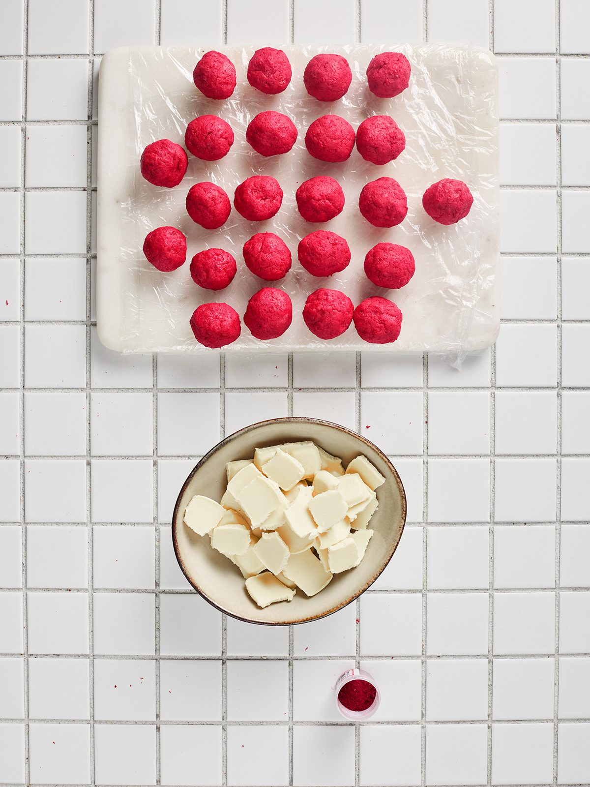 Rows of rolled red velvet truffle balls arranged on a plastic-wrapped board before dipping.