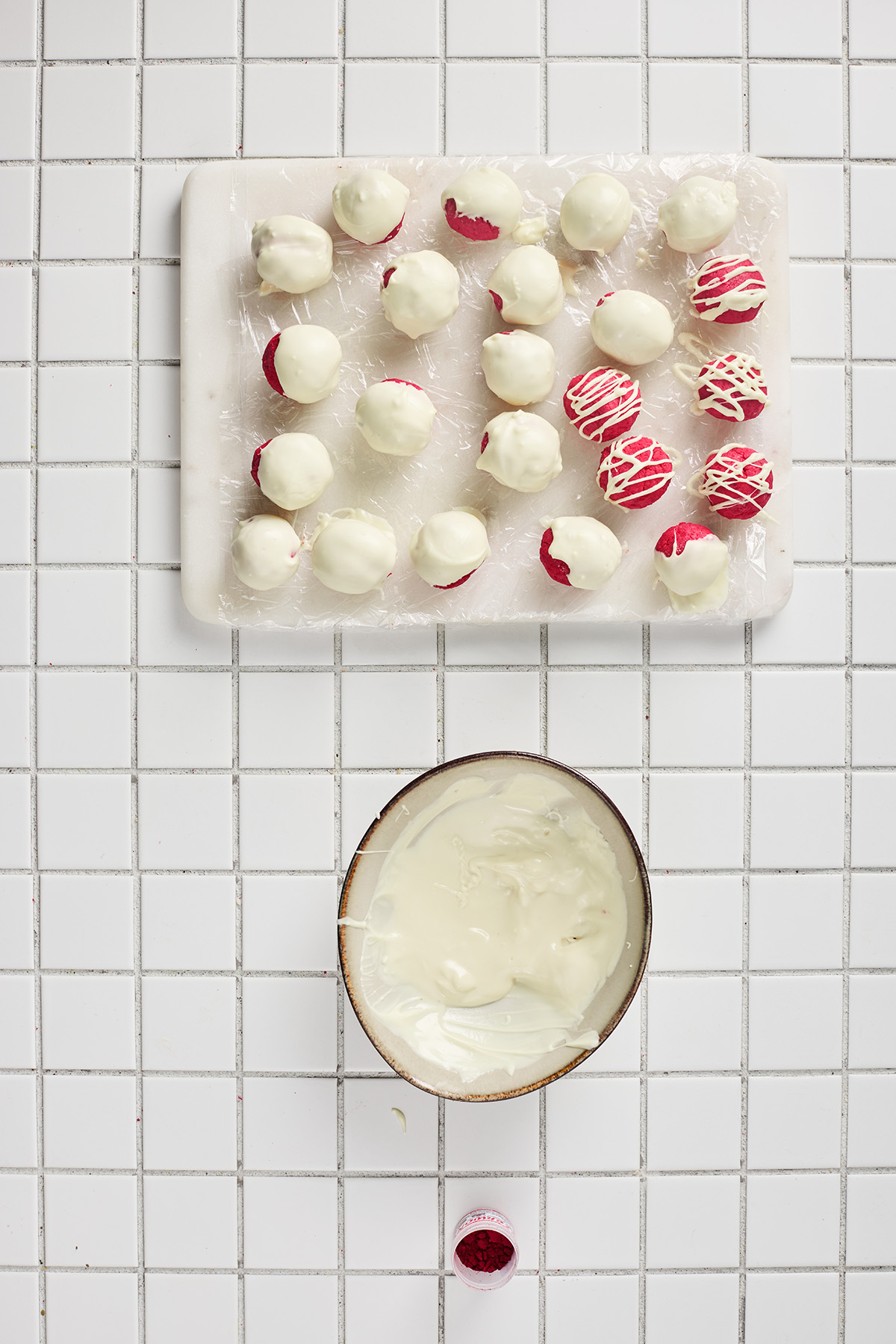 Red velvet truffle balls coated in white chocolate and set on a board, with some decorated using a white chocolate drizzle.