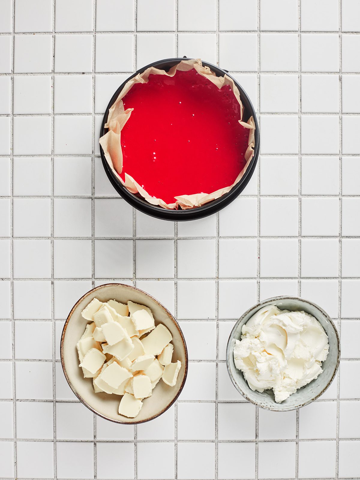 Unbaked red velvet cake batter poured into a parchment-lined round pan on a white tiled surface.