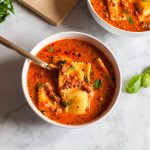 Bowl of million dollar ravioli soup with cheese ravioli, creamy tomato broth, ground beef, and fresh parsley on top.