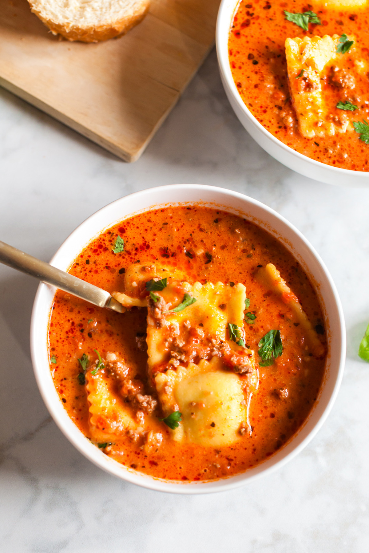 Close-up of cheesy ravioli in creamy tomato soup with ground beef and fresh herbs, served in a white bowl.
