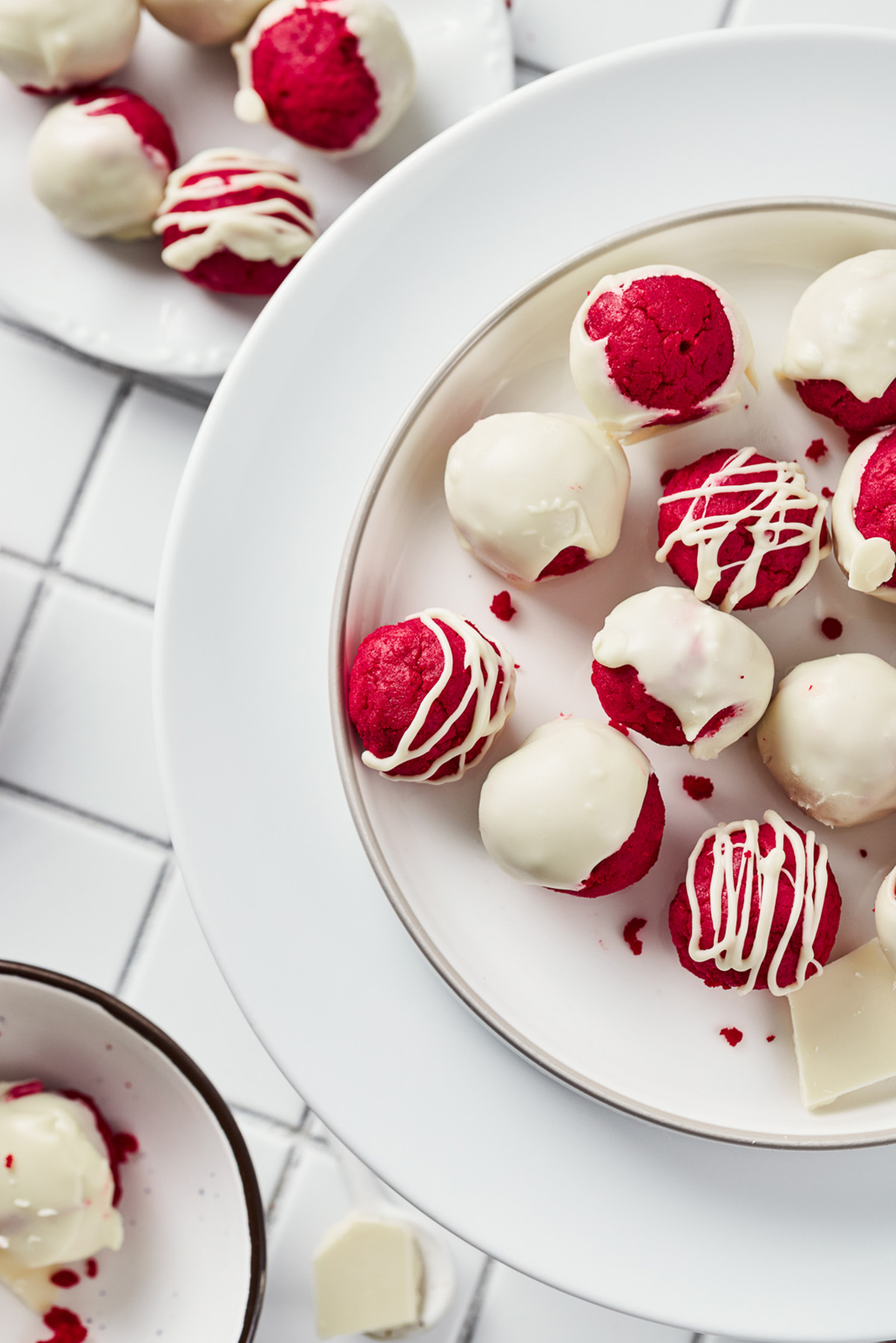 Plate of bright red velvet truffles coated in white chocolate with a mix of smooth and drizzled finishes.
