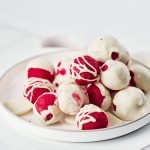 Side view of red velvet truffles stacked on a plate, half dipped in white chocolate with decorative white chocolate drizzle.