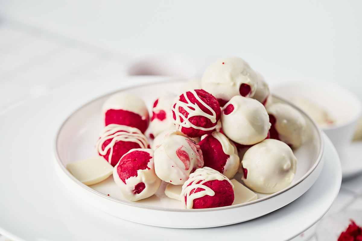 Side view of red velvet cake truffles stacked on a plate, half dipped in white chocolate with decorative white chocolate drizzle.