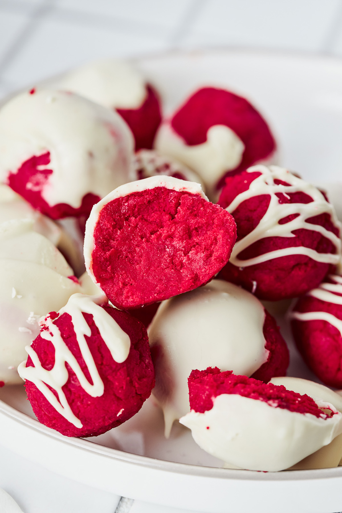 Close-up of red velvet cake truffles with white chocolate shells, including one truffle bitten open to show the soft red velvet cake center.
