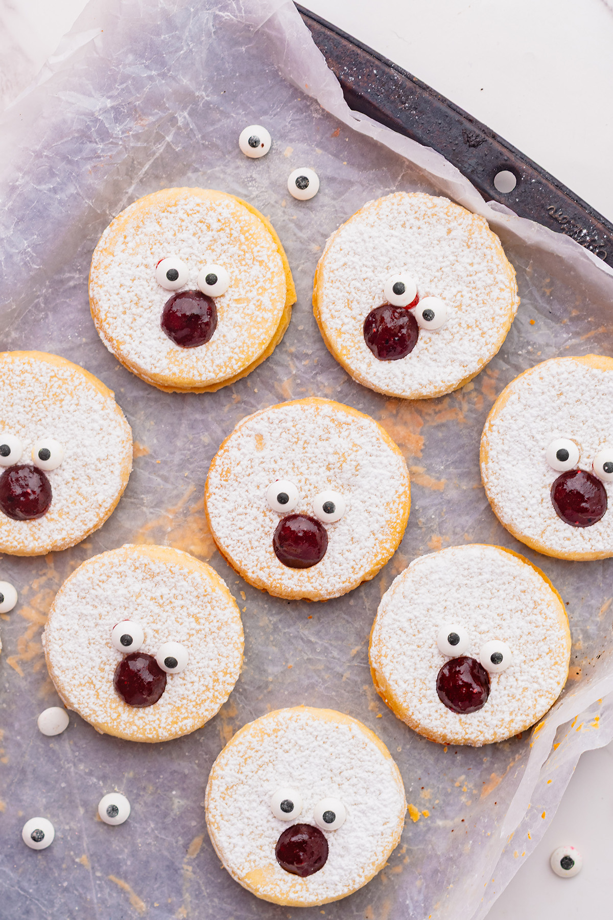 Powdered sugar–dusted linzer cookies topped with candy eyes and a strawberry jam nose to create Rudolph faces for reindeer linzer cookies.