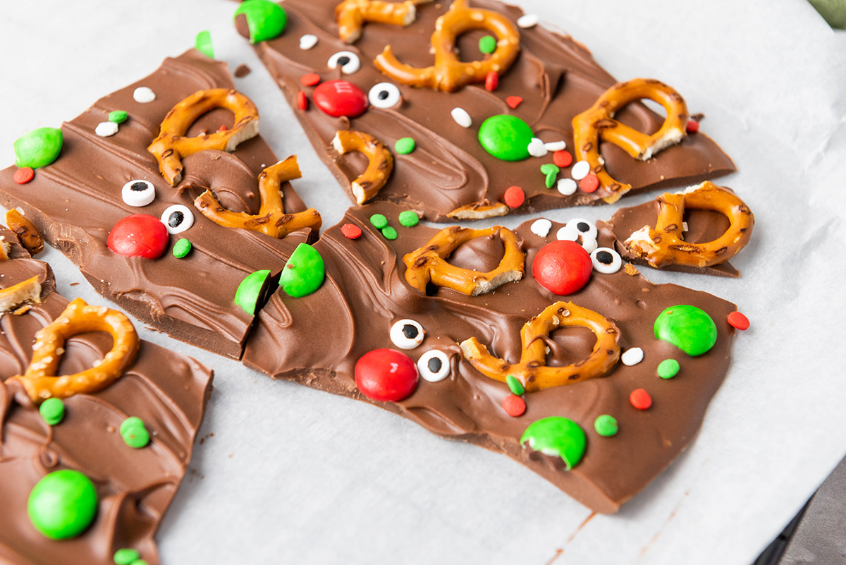 Close-up of chocolate reindeer bark broken into pieces with pretzel antlers, red noses, and holiday sprinkles.