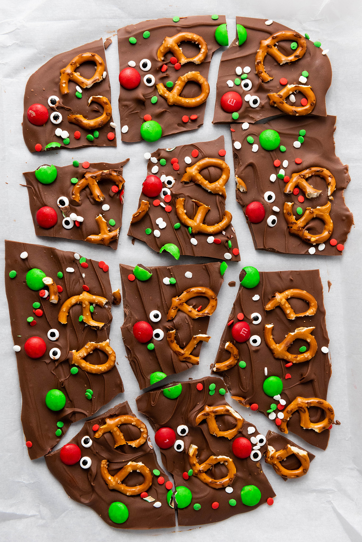 Broken pieces of chocolate reindeer bark topped with pretzels, red and green M&M’s, candy eyes, and holiday sprinkles.