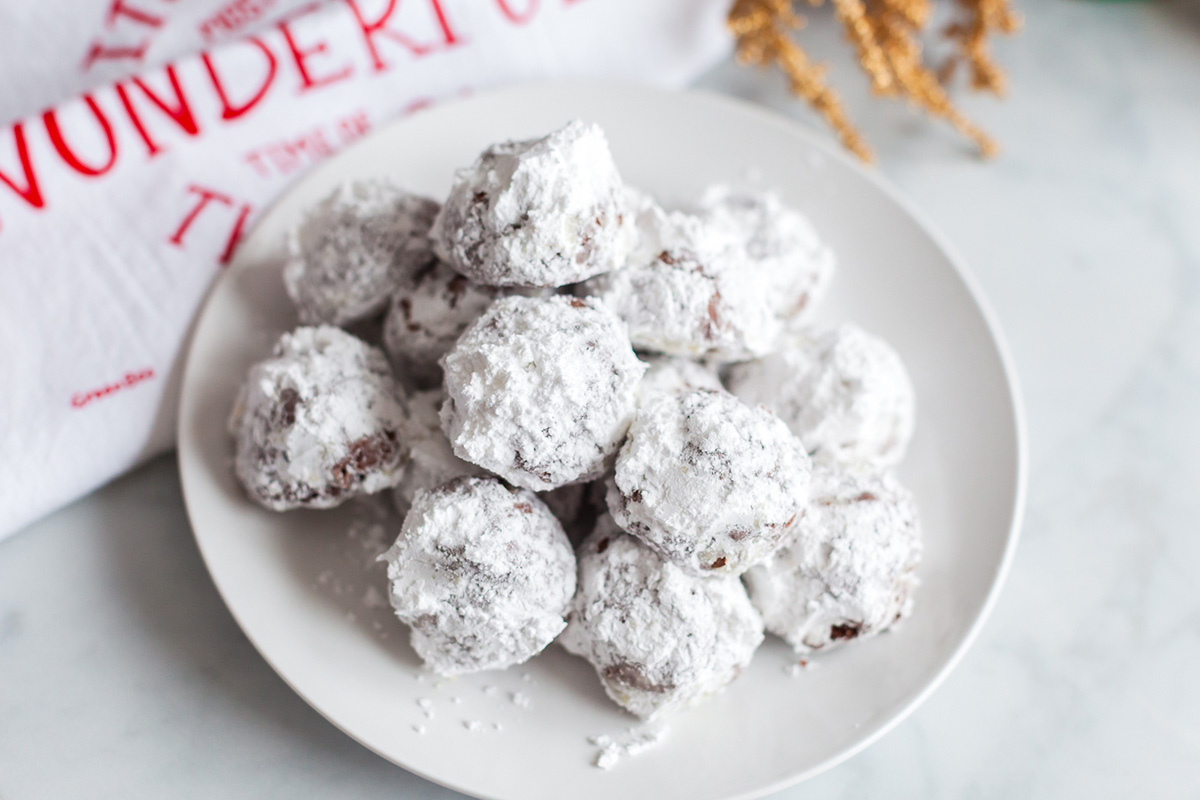 Close-up of powdered sugar–coated double chocolate snowball cookies piled on a white plate.
