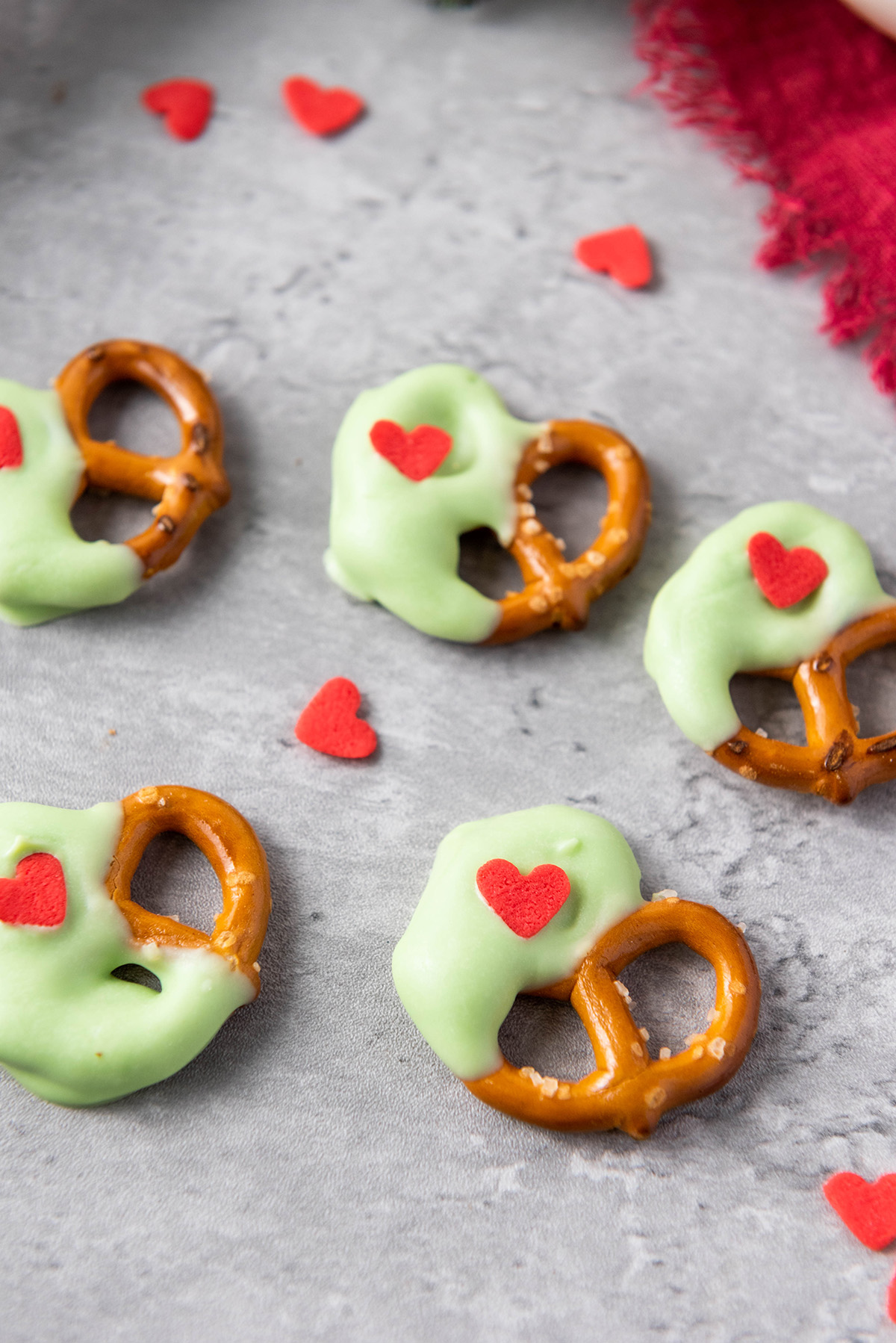 A close-up shot of Grinch-themed pretzels showing the glossy green candy coating and red heart sprinkles.