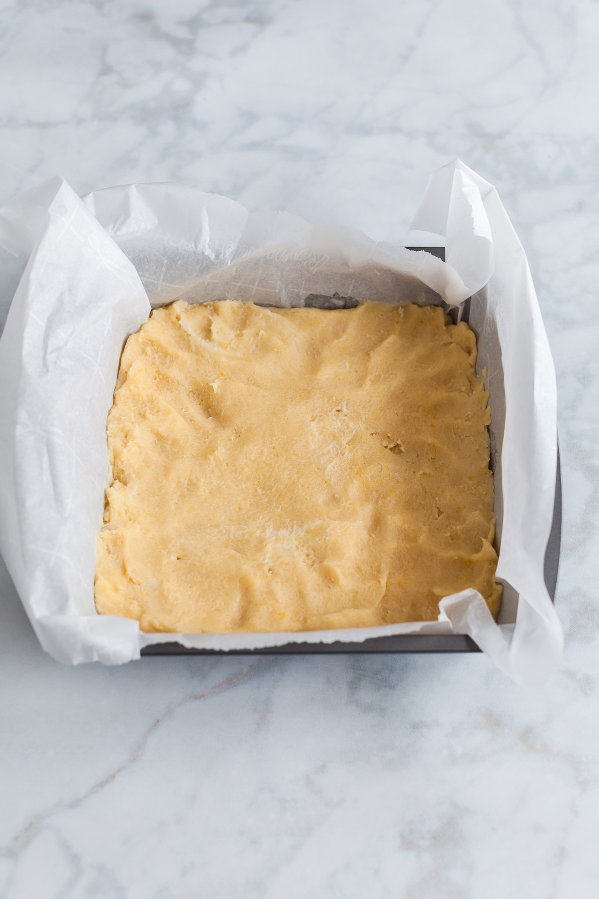 Sugar cookie bar dough pressed evenly into a parchment-lined square baking pan.