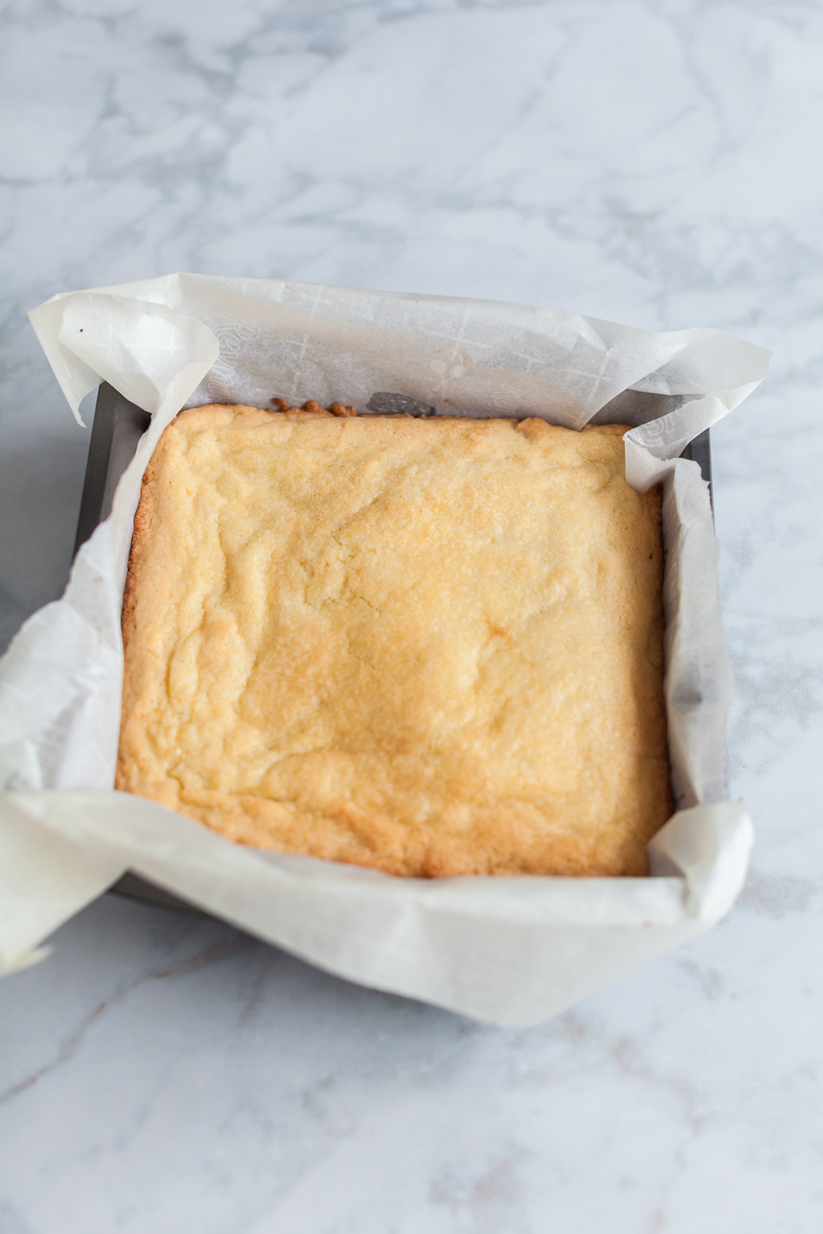 Baked sugar cookie bar base cooling in a parchment-lined square baking pan.