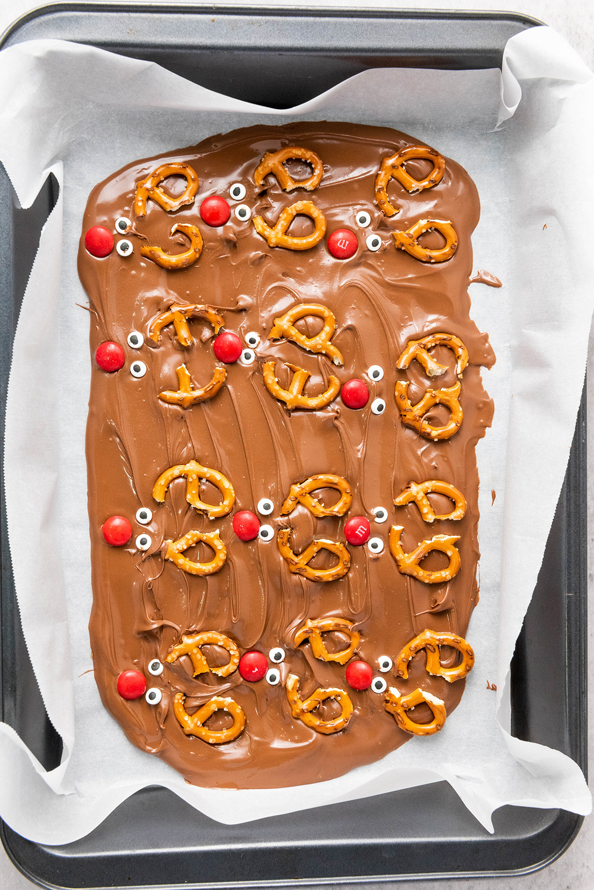 Pan of chocolate reindeer bark topped with pretzels, candy eyes, and red M&M noses to look like Rudolph.