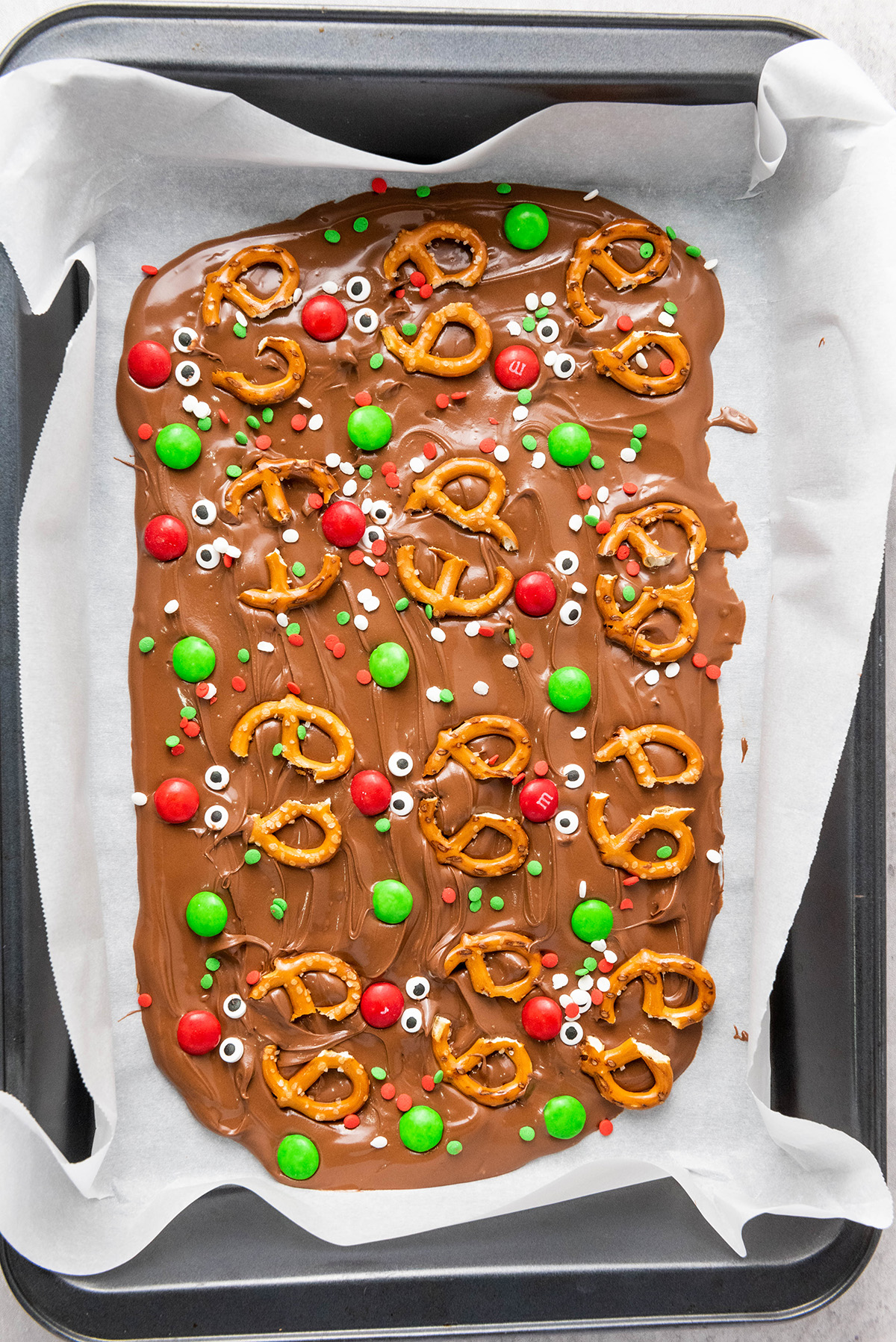 Finished chocolate reindeer bark decorated with pretzels, candy eyes, red and green M&M’s, and sprinkles before chilling.