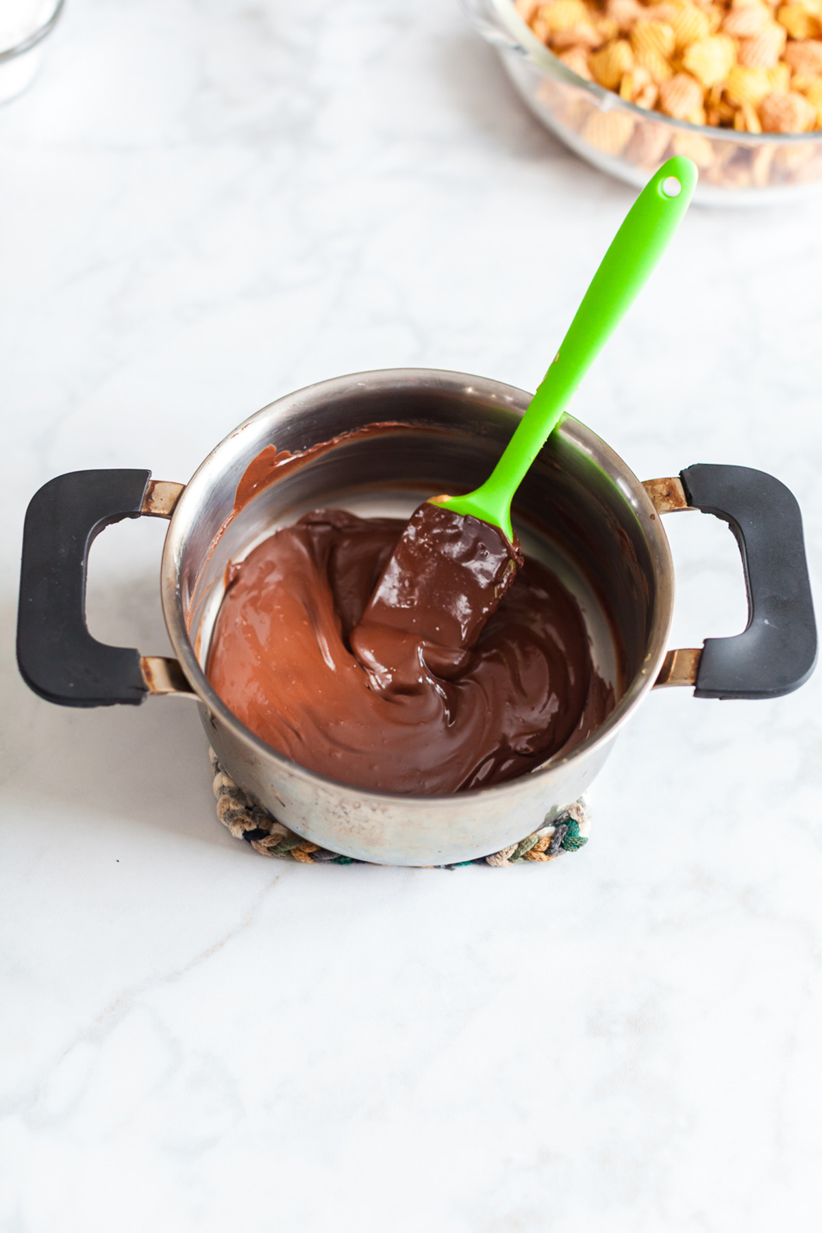 Crispix cereal stirred with melted chocolate and peanut butter in a mixing bowl.