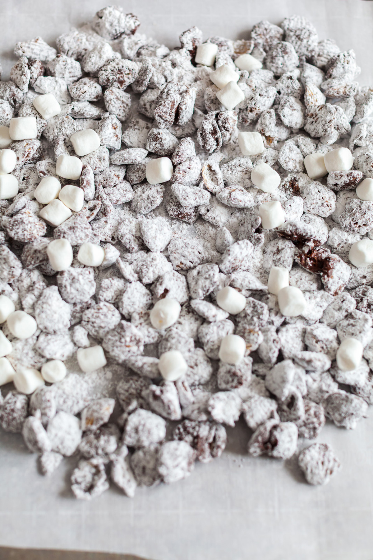 Freshly coated Crispix puppy chow cooling on parchment paper with powdered sugar and marshmallows.