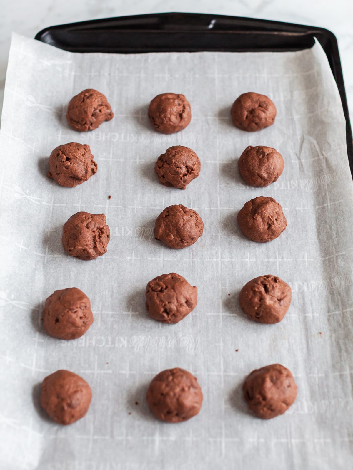 Baked chocolate snowball cookies cooling on a parchment-lined baking sheet before coating in powdered sugar.