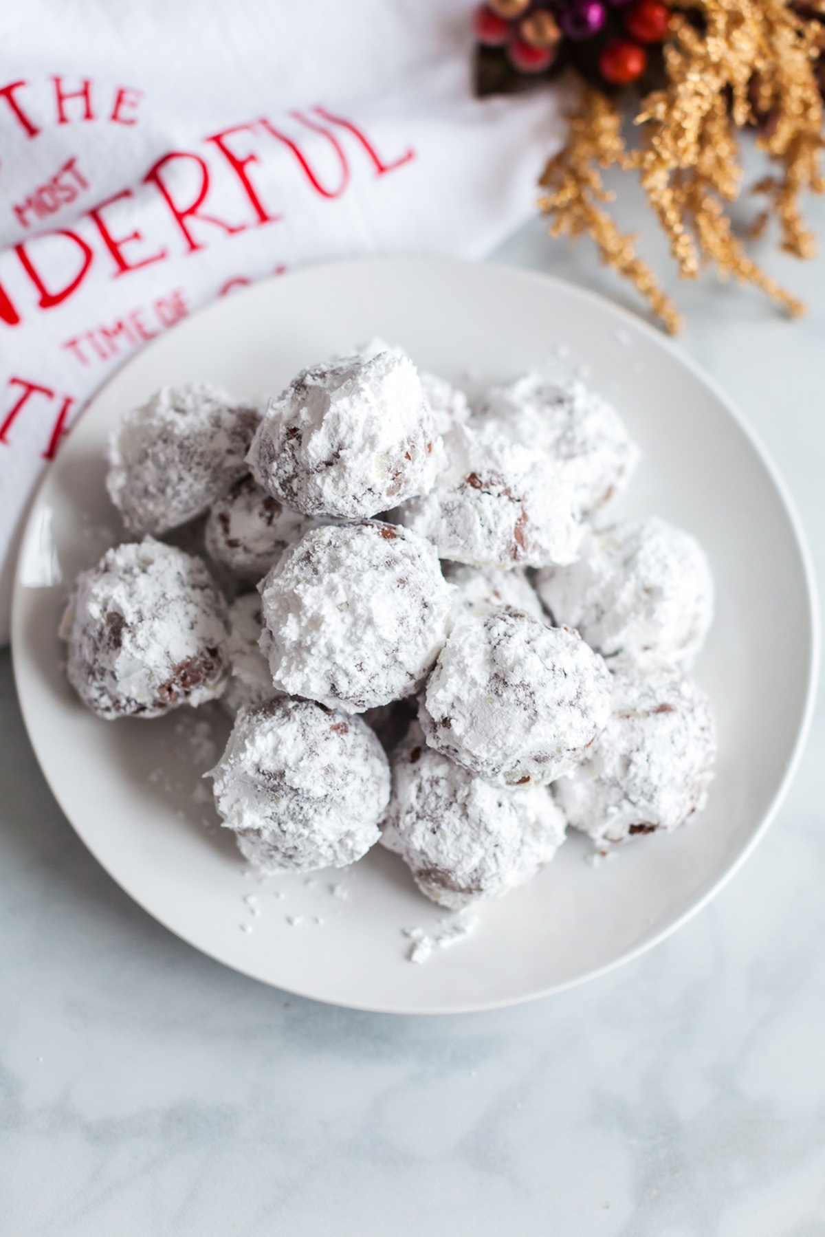 Double chocolate snowball cookies stacked on a white plate, coated generously in powdered sugar.