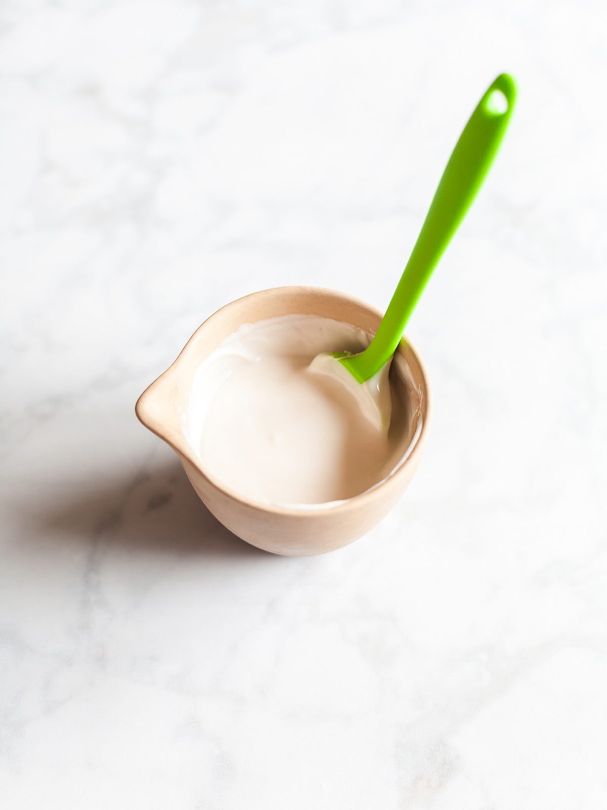A small bowl filled with melted white chocolate and a green spatula resting inside.