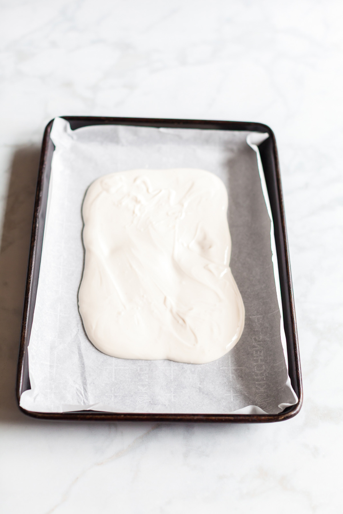 Melted white chocolate spread into a rectangle on a parchment lined sheet pan before adding color or toppings.
