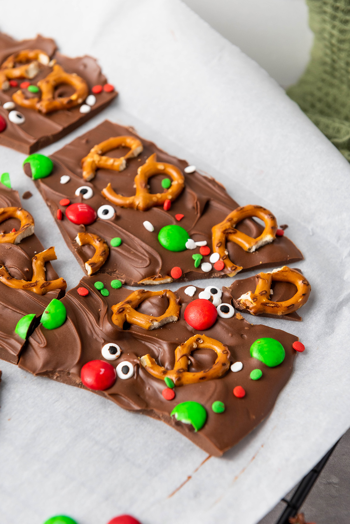Pieces of chocolate reindeer bark arranged on parchment paper, showing pretzel antlers, red M&M noses, and candy eyes.