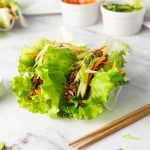 Korean ground beef lettuce wraps topped with sesame seeds, carrots, cucumber, and green onions.