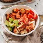Close-up of a blackened chicken and sweet potato bowl with juicy tomatoes, creamy avocado, and roasted chicken pieces.