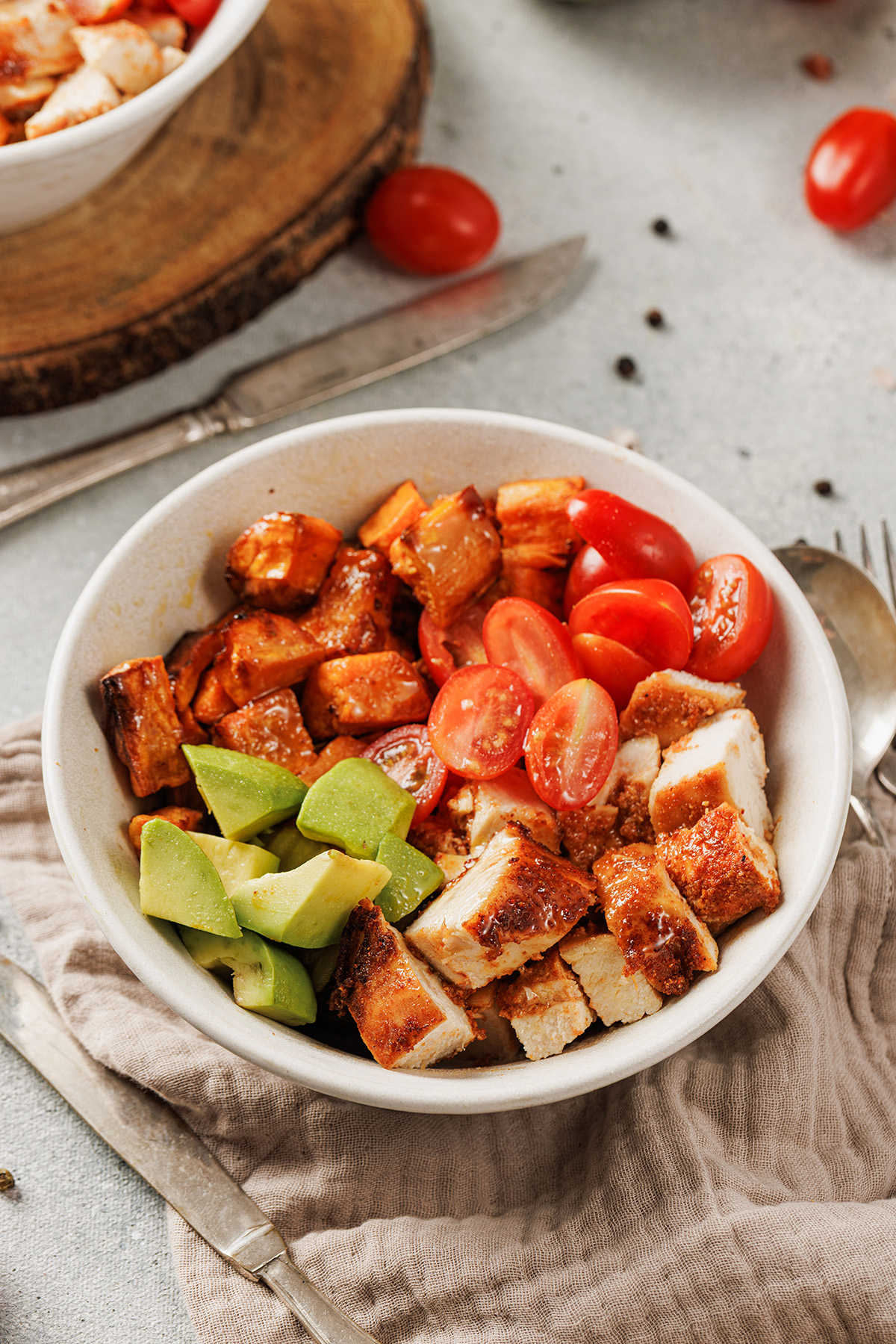 Blackened chicken and sweet potato bowl topped with fresh cherry tomatoes and diced avocado.