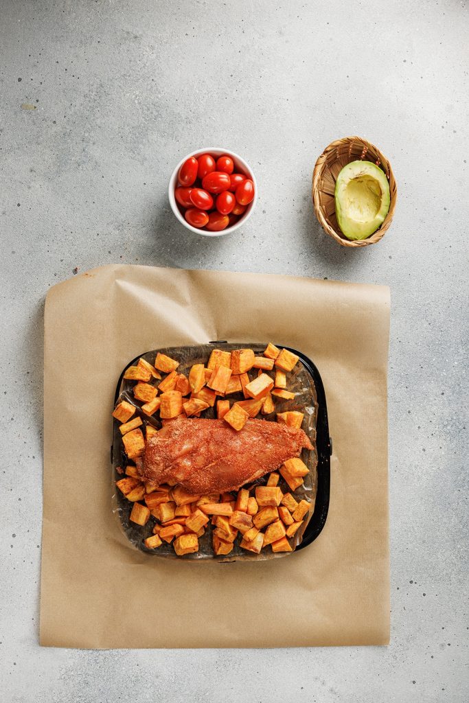 Blackened chicken and sweet potato bowls made with bold spices, roasted sweet potatoes, fresh tomatoes, and creamy avocado. Easy and satisfying. Blackened chicken breast and cubed sweet potatoes arranged on a parchment-lined baking pan before roasting.