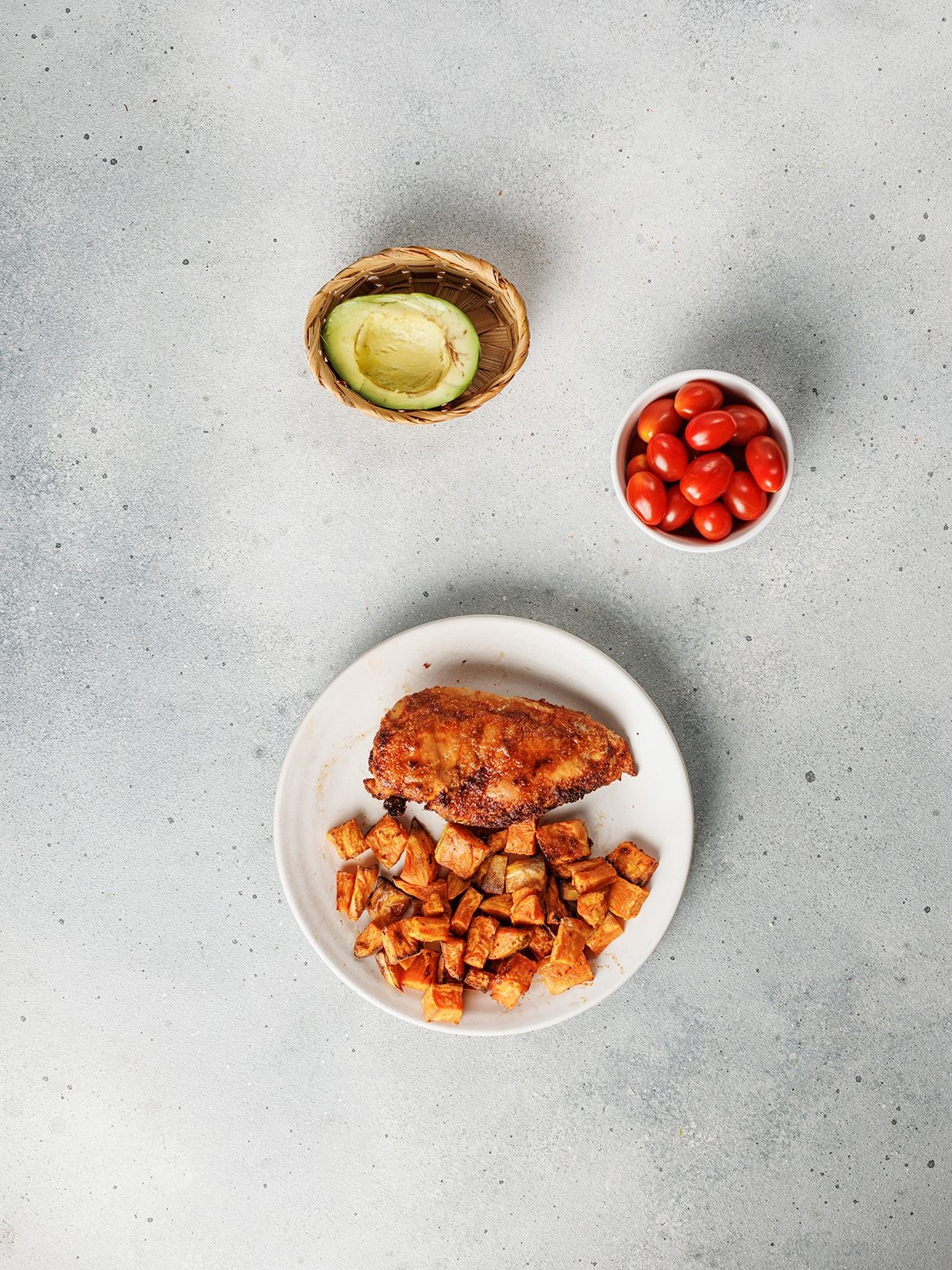 Blackened chicken and sweet potato bowls made with bold spices, roasted sweet potatoes, fresh tomatoes, and creamy avocado. Easy and satisfying. Oven-roasted blackened chicken breast served with golden roasted sweet potatoes on a plate.