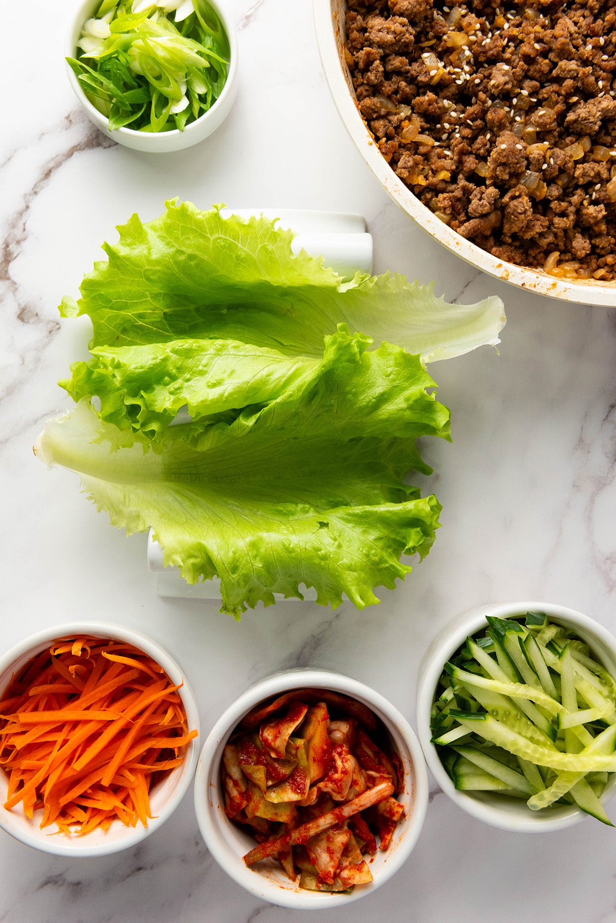 Butter lettuce leaves arranged with shredded carrots, cucumber, and kimchi for assembling lettuce wraps.