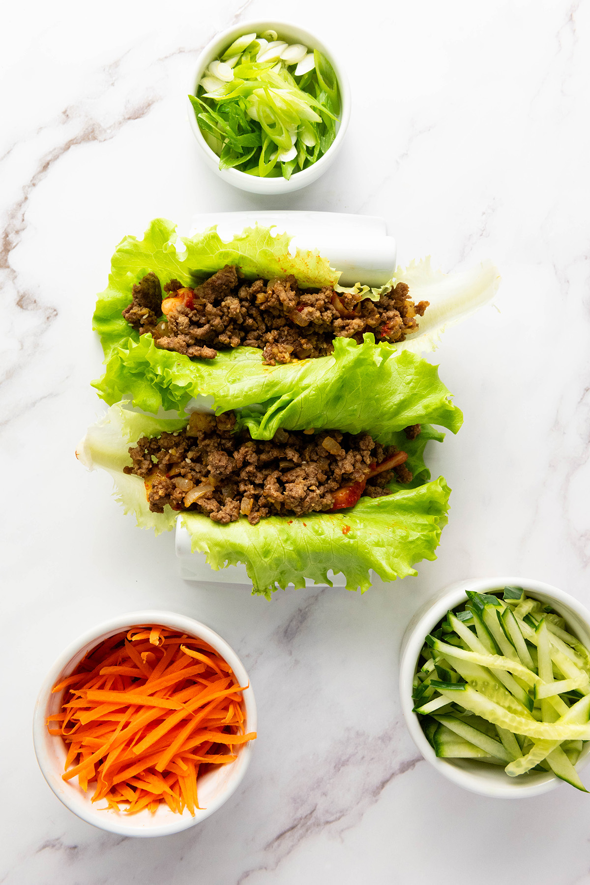 Korean ground beef spooned into crisp lettuce leaves with fresh vegetables and green onions.