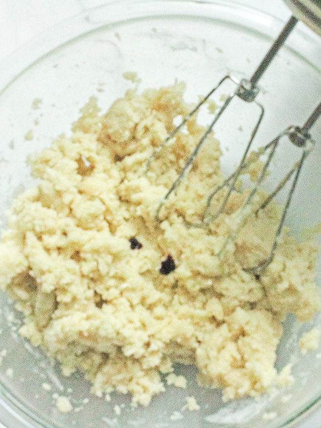 Sugar cookie dough being mixed with a hand mixer in a glass bowl.