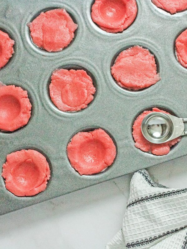 Pink sugar cookie dough pressed into a mini muffin pan to form cookie cups.