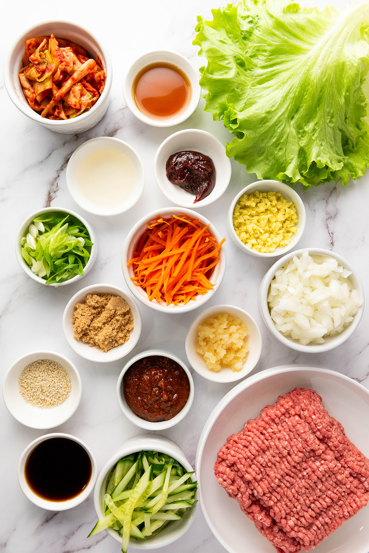 Ingredients for Korean ground beef lettuce wraps including ground beef, gochujang, soy sauce, garlic, ginger, vegetables, and butter lettuce.