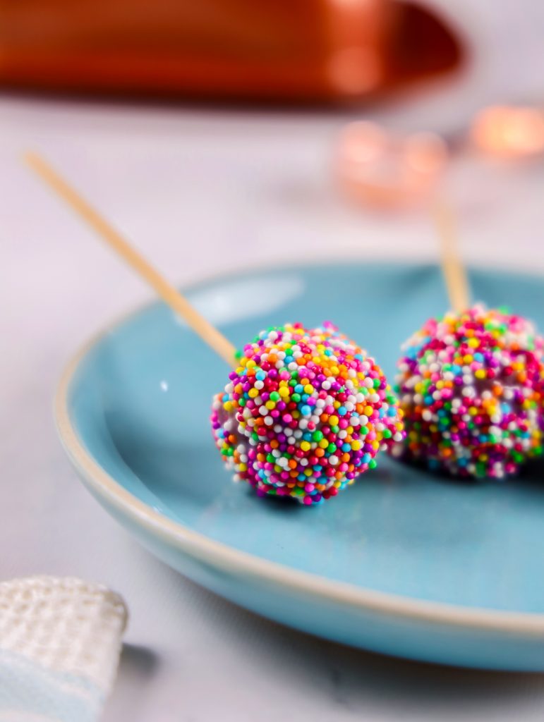 Close up of a red velvet cake pop covered in white chocolate and sprinkles.