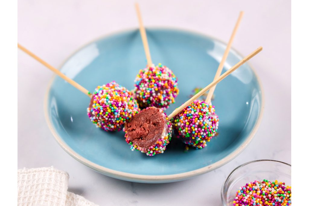 Finished red velvet cake pops coated in white chocolate and sprinkles.