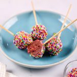 Finished red velvet cake pops coated in white chocolate and sprinkles.