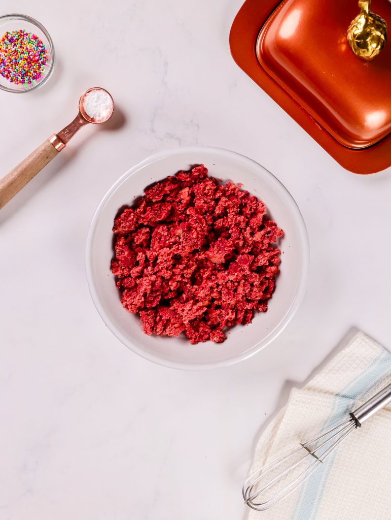 Crumbling homemade red velvet cake into a bowl to prepare the cake pop mixture.