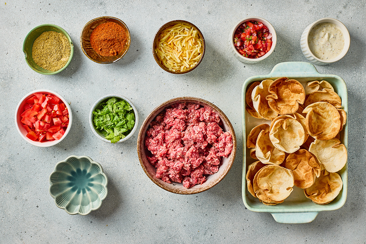 Ingredients for taco ranch bites including ground beef, taco seasoning, ranch seasoning, tortilla scoop chips, cheese, tomatoes, and cilantro.