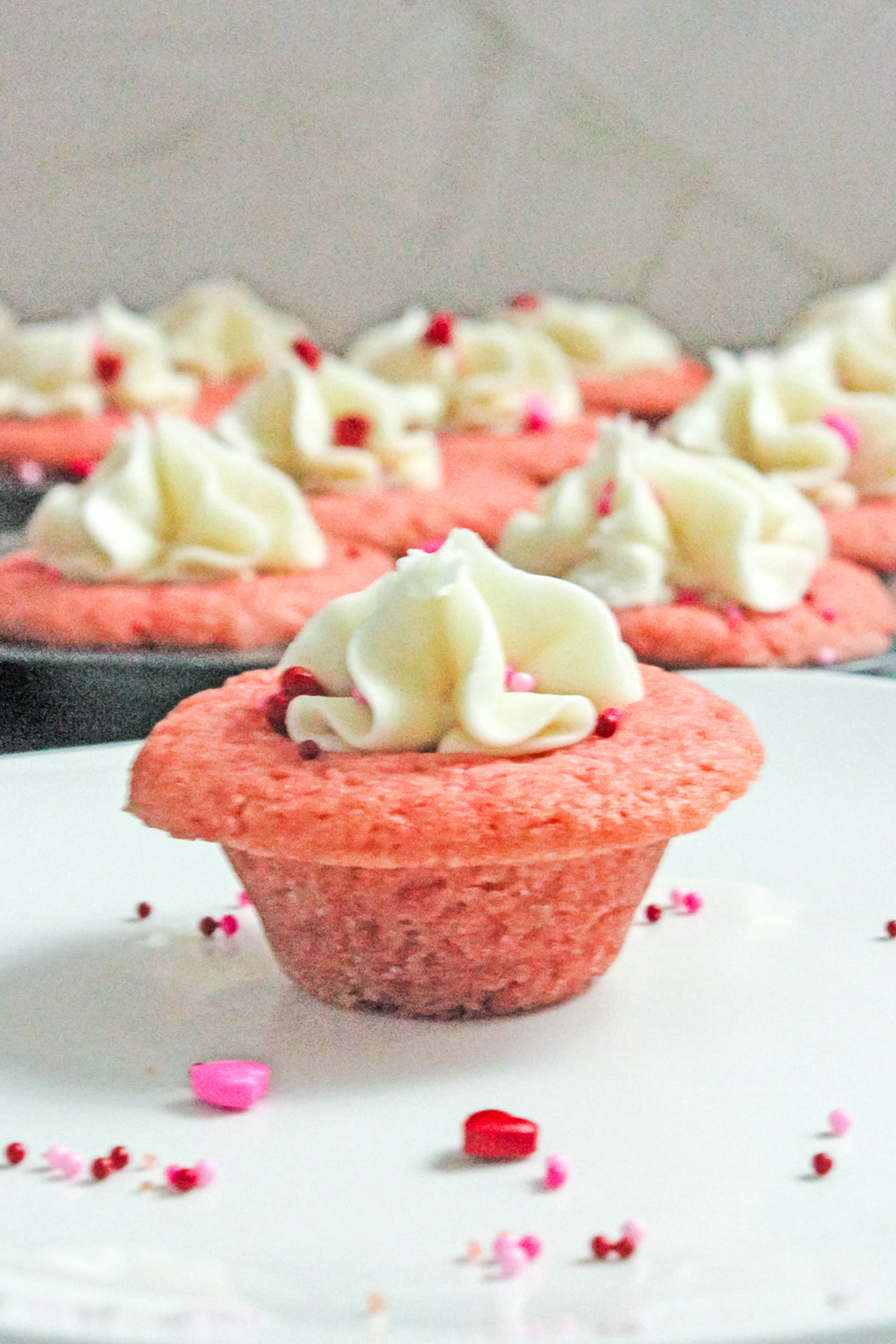 Valentine’s Day sugar cookie cup with vanilla frosting and pink sprinkles on a white serving plate.