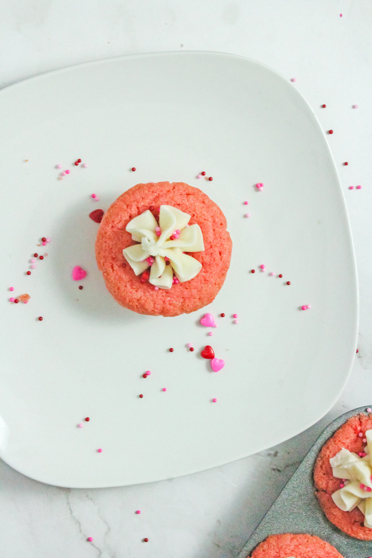 Valentine’s Day sugar cookie cup with vanilla frosting and pink sprinkles on a white serving plate.